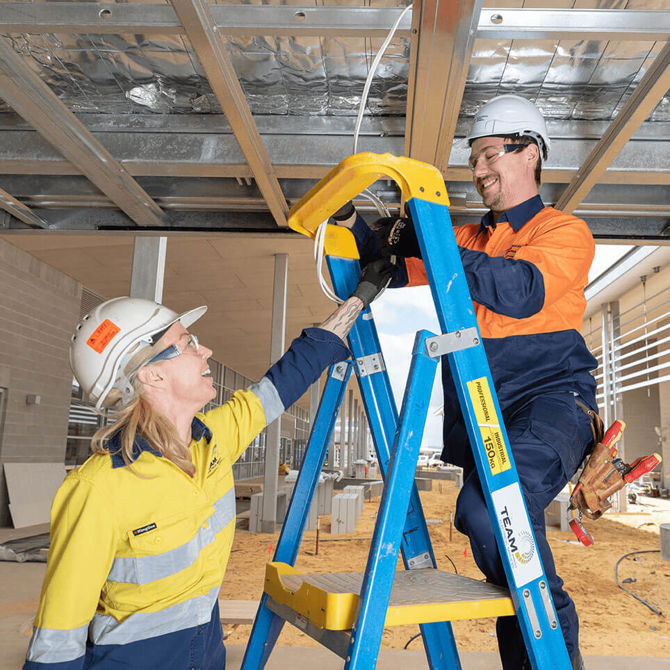 Female electrician working with a colleague on a ladder installing wiring