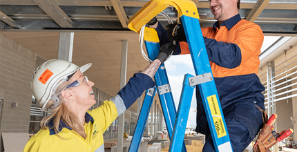Male and female electrician wearing hard hats and working on a blue ladder