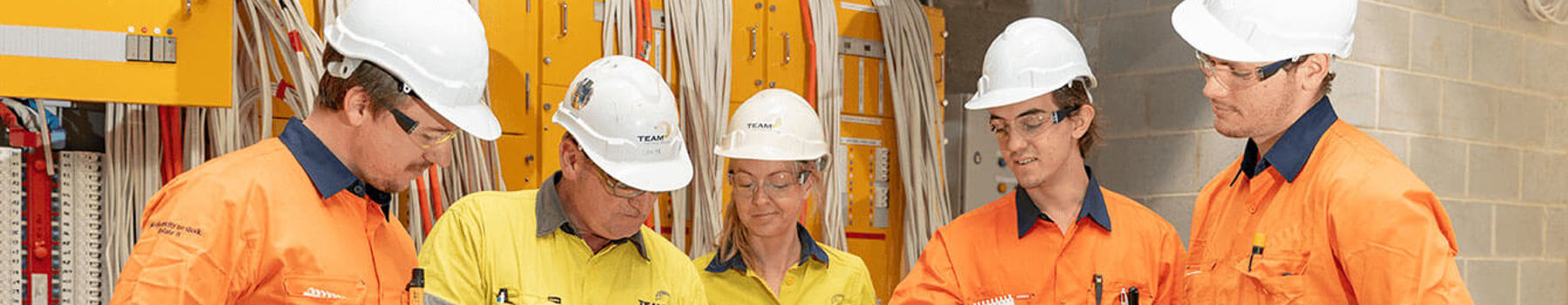 Host employer mentoring apprentice electricians. Discussing work plans and safety, looking at a hardcopy plan.