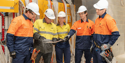 Host employer mentoring apprentice electricians. Discussing work plans and safety, looking at a hardcopy plan. 